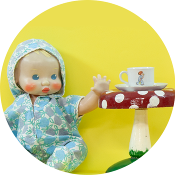 A baby doll sits beside a mushroom stool with a tea set