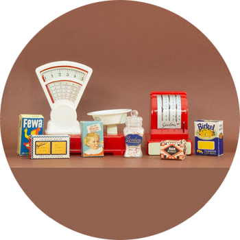 Lektillbehören i en miniatyrhandelsbod, en våg, en kassamaskin och varuförpackningar